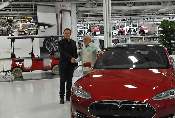 инженер и исследователь Илон Маск на заводе электромобилей, здоровается за руку с рабочим.