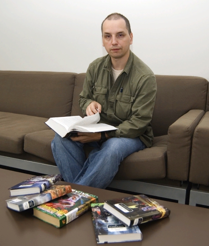 Писатель Ник Перумов сидит на диване с книгами